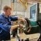 A person wearing PPE operating a lathe machine