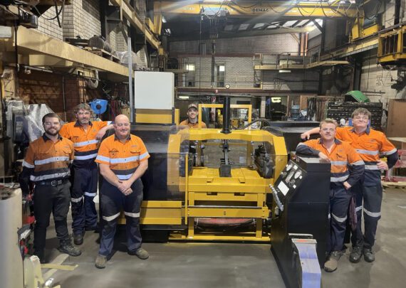 A group of workers wearing safety uniform beside a stationary track press machine